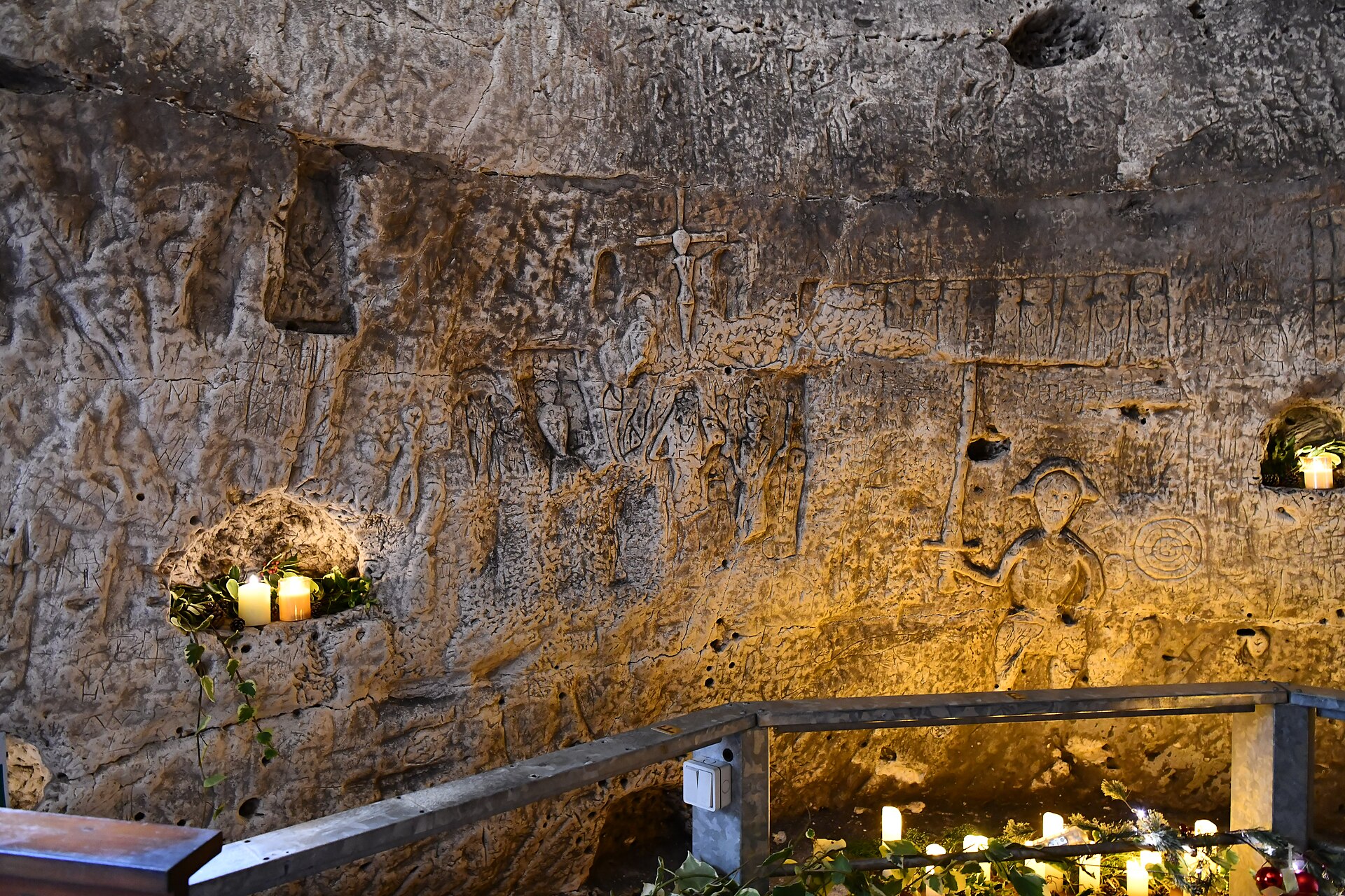 Medieval carvings of saints and crosses inside Royston Cave, lit by a single lantern